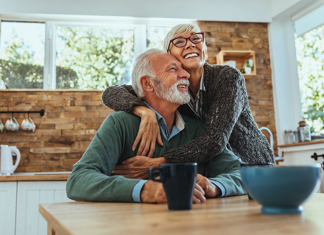Medicare - Loving Elderly Couple Embrace Each Other in Their Kitchen